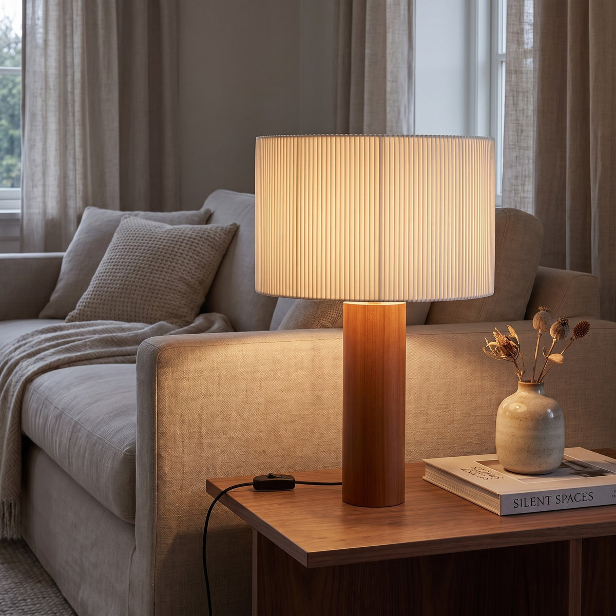Brisenne pleated table lamp lit beside a linen sofa