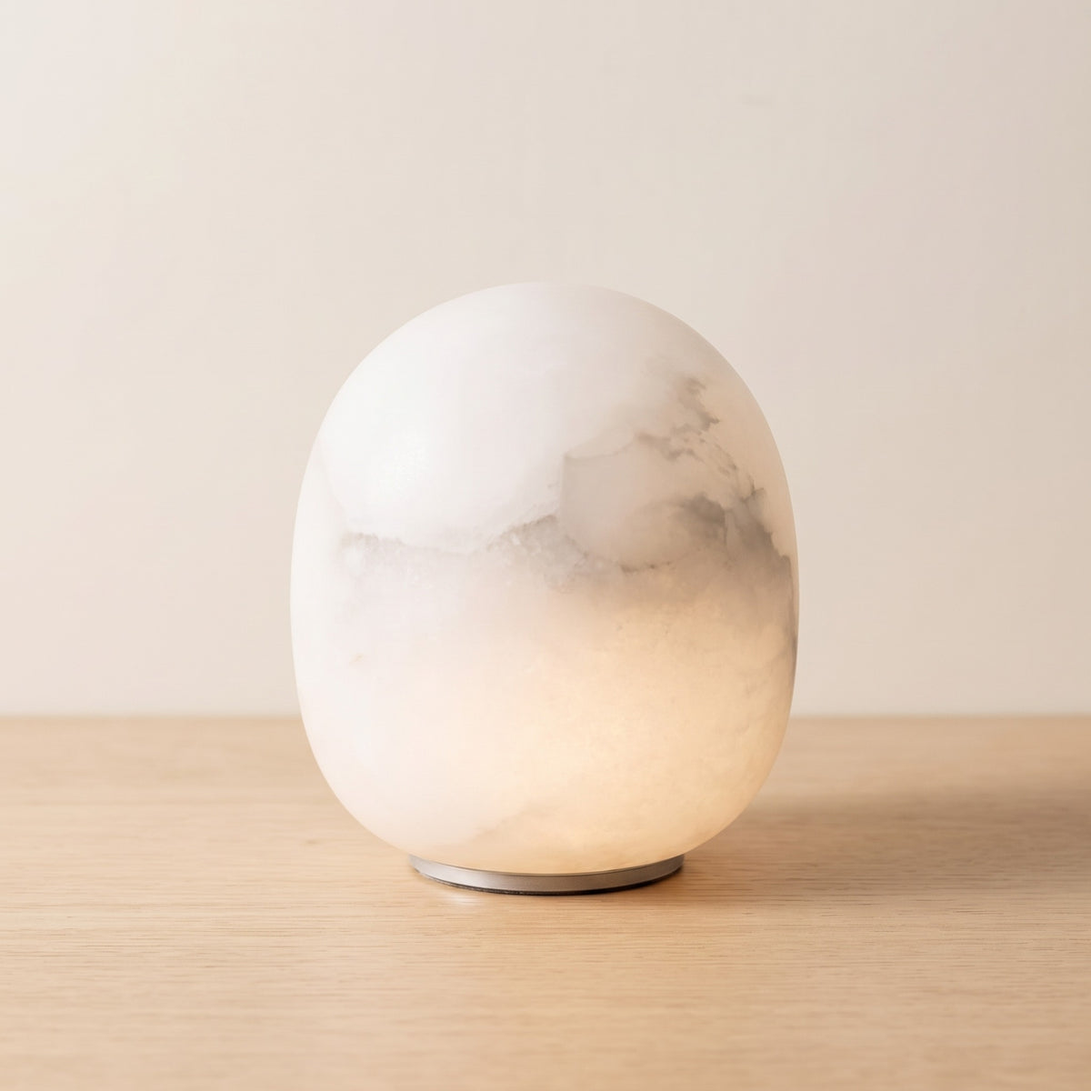 Calmora tall alabaster pebble lamp glowing on an oak surface