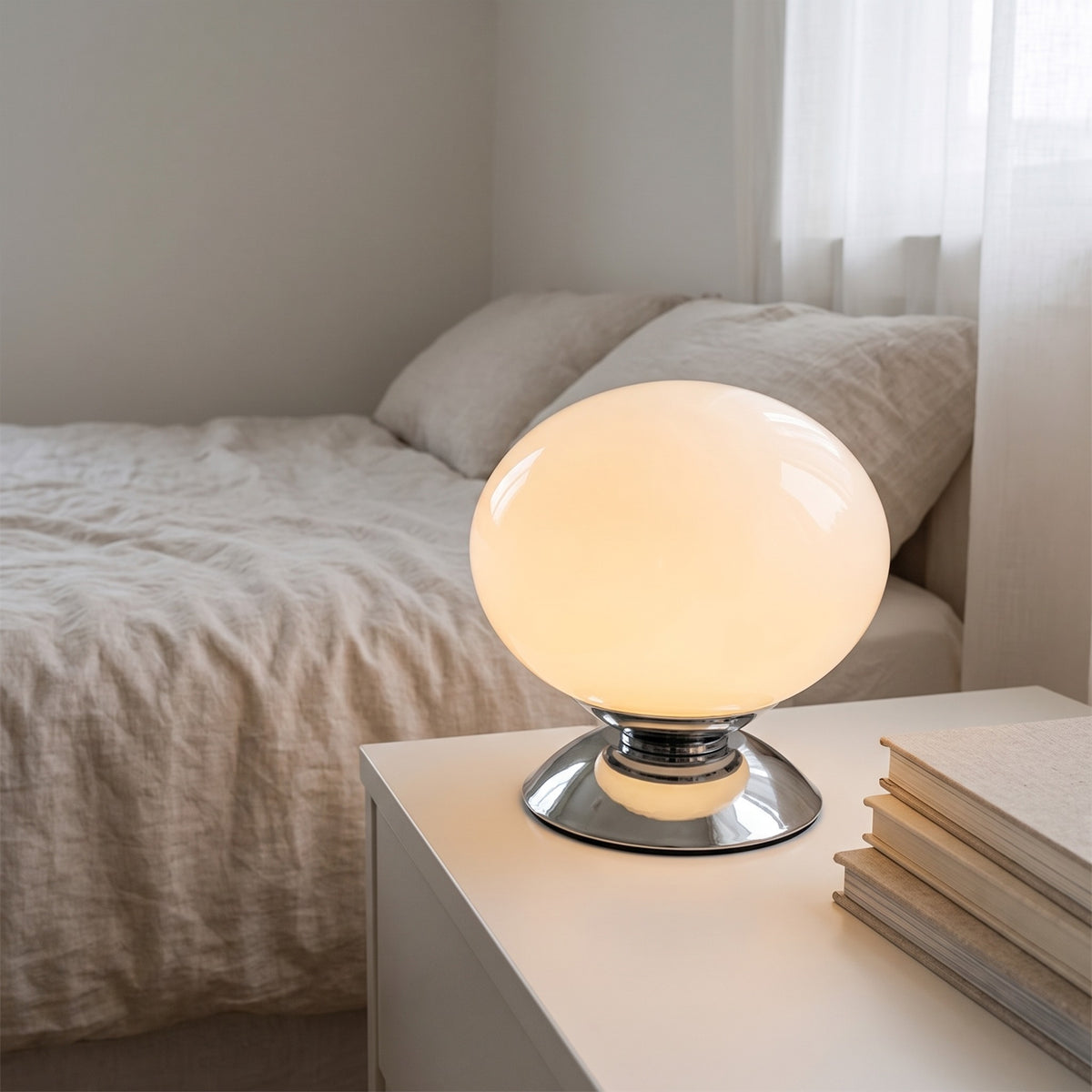 Pearl white Pastelle globe lamp lit on a bedside table